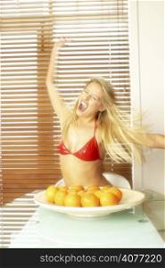 20s attractive woman going crazy in front of a bowl of oranges. Funny movement shot of female with long blond hair.