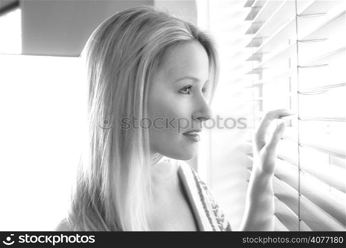 20s woman in her home looking out through her venison blinds in black and white.