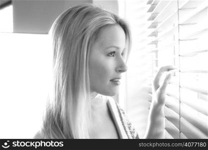 20s woman in her home looking out through her venison blinds in black and white.