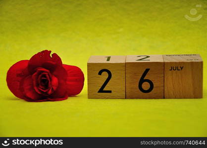26 July on wooden blocks with a red flower on a yellow background