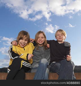 3 children sitting on low wall, smiling