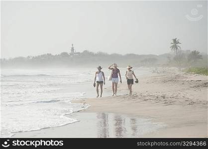 ""3 women in shorts and hats walking on the beach"
