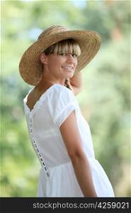 30 years old blonde woman wearing a white dress and a straw hat walking in the nature