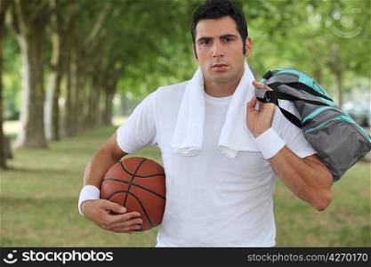30 years old sportyman holding a basket ball and a sports bag