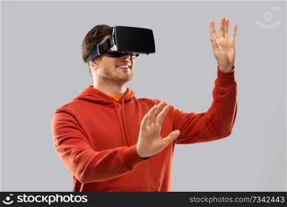 3d technology, virtual reality, entertainment and people concept - happy young man in vr glasses playing game and touching something imaginary over grey background. happy man in virtual reality headset or vr glasses