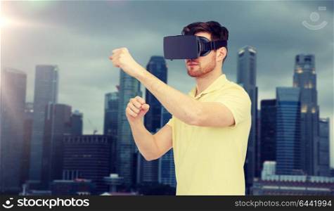 3d technology, virtual reality, entertainment and people concept - young man with virtual reality headset or 3d glasses playing game and fighting over singapore city background. man in virtual reality headset or 3d glasses