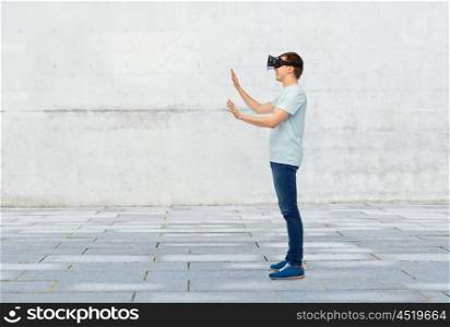3d technology, virtual reality, entertainment, cyberspace and people concept - happy young man with virtual reality headset or 3d glasses playing game and touching something over street background