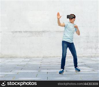 3d technology, virtual reality, entertainment, cyberspace and people concept - young man with virtual reality headset or 3d glasses playing game and fighting over street background