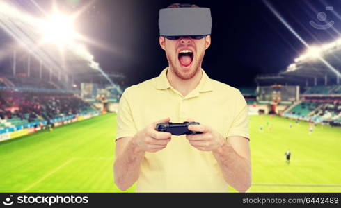 3d technology, virtual reality, sport, entertainment and people concept - man in virtual reality headset or 3d glasses playing with game controller gamepad over football field on stadium background. man in virtual reality headset over football field