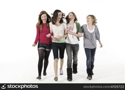 4 teenage girls linking arms walking towards camera smiling
