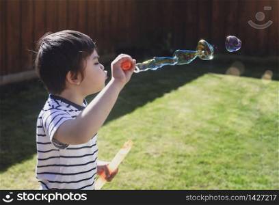 4 years old kid blowing soap bubble wand, Child boy stay at home playing in the garden in sunny day spring during self-isolation and quarantine. Coronavirus outbreak and flu covid epidemic