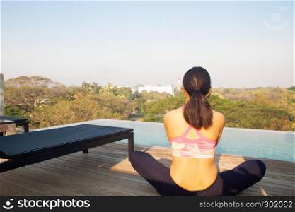 40s woman doing yoga near swimming pool on the roof top. Healthy lifestyle concept