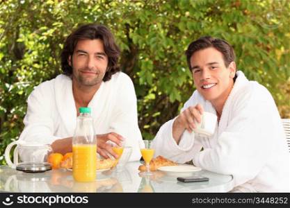 45 years old man and a 20 years old man dressed in bathrobe drinking coffee at breakfast