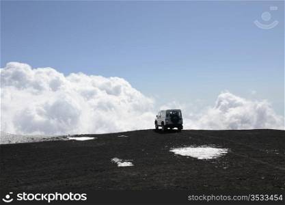 4x4 Vehicle on lava and snow at the top of Mt Etna volcano - clouds background. off-road Vehicle on Mt Etna volcano