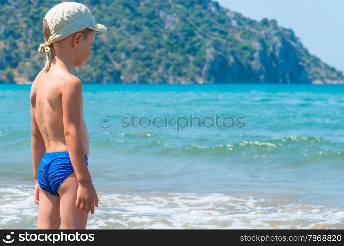 5 years old boy in swimming trunks is looking at waves