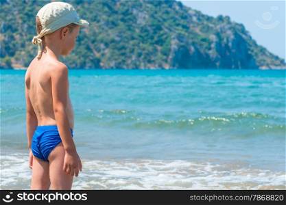5 years old boy in swimming trunks is looking at waves