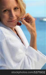 50 years old blonde woman dressed in bathrobe in front of the sea taking cherries in her fingers