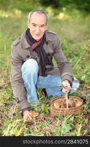 65 years old man kneeling and picking mushrooms