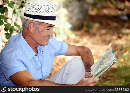65 years old man sitting in the grass and watching a book