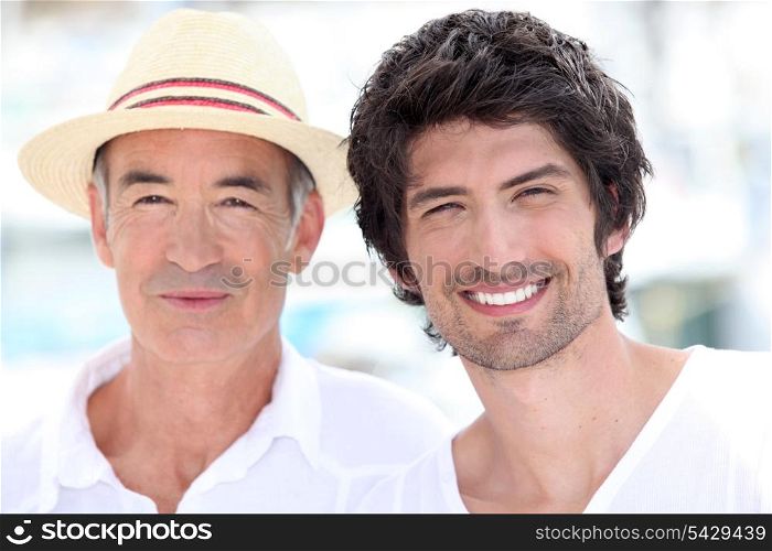 65 years old man wearing a straw hat and a 25 years old man posing in a summer vacation atmosphere
