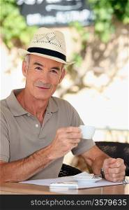 65 years old man wearing a straw hat and drinking a tea cup on a cafe terrace