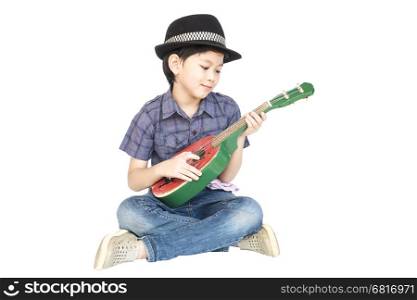 7 years old Asian boy is sitting and playing ukulele isolated over white.
