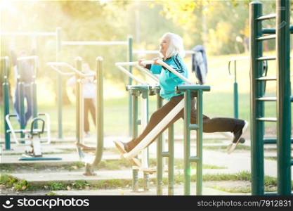 70 years old Senior Woman doing Exercises for Legs Outdoors in the Bright Autumn Evening