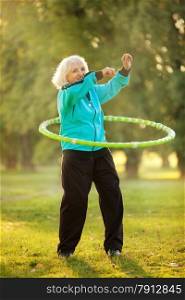 70 years old Senior Woman doing Exercises with the Plastic Hoop at the Green Meadow in the Bright Autumn Evening