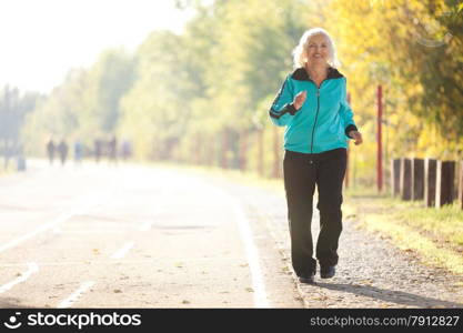 70 years old Senior Woman Jogging at the Pedestrian Walkway in the Bright Autumn Evening