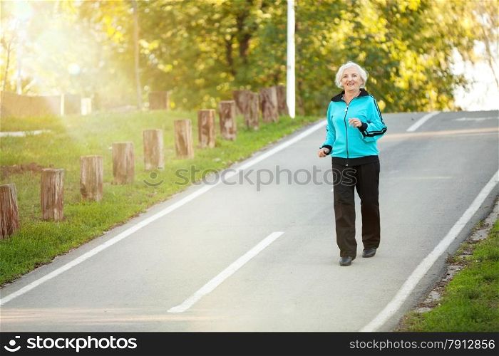 70 years old Senior Woman Jogging at the Pedestrian Walkway in the Bright Autumn Evening
