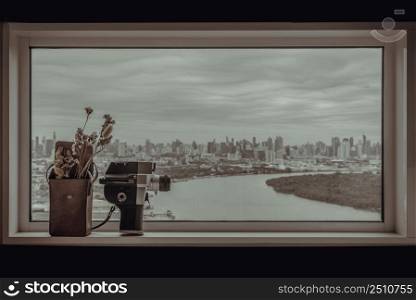 8mm vintage movie camera and Dried flowers in Mini brown leather bag by the glass wall with city and river view. Vintage tone style, Copy space for text, Selective focus.