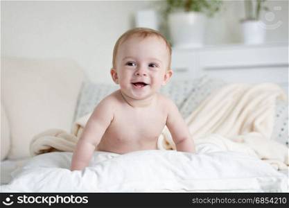 9 month old happy baby crawling over pillows on bed