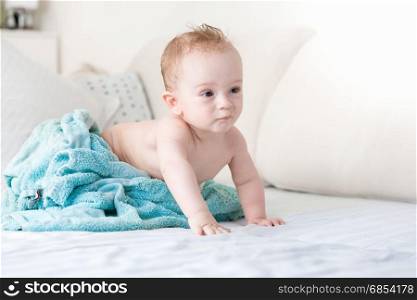 9 months baby boy under blue towel on bed with white sheets