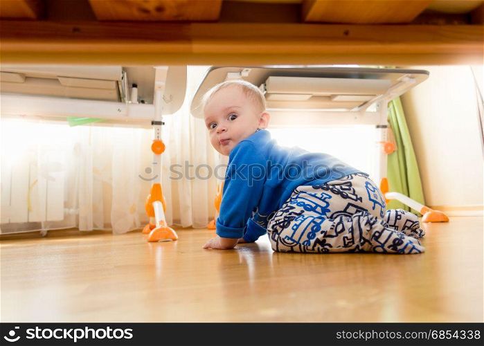9 months old baby boy crawling under the bed at bedroom