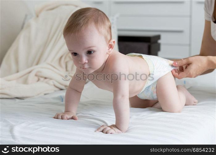 9 months old baby boy in diapers crawling on bed