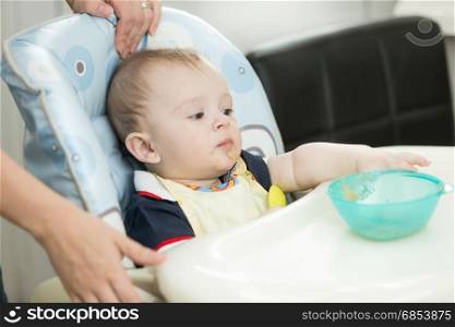 9 months old baby boy sitting in highchair and reaching for dish
