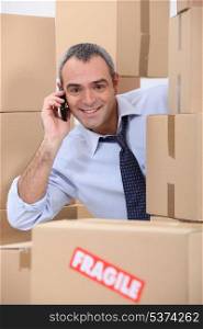 a 40-45 years old employee calling someone in a room full of cardboard boxes