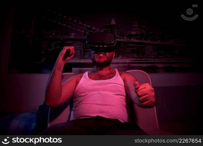 A 40-year-old unshaven overweight man watches TV with VR glasses, shows various emotions, gets angry. lazy middle-aged man.. A 40-year-old unshaven overweight man watches TV with VR glasses, shows various emotions, gets angry. lazy middle-aged man