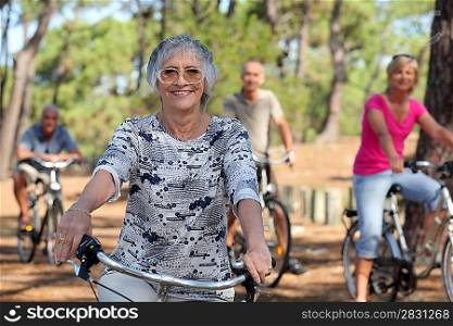 a 65 years old woman in first plan and three other people doing bike in the forest