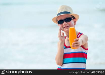 A 7 year old boy shows a protective sun cream and smears his skin on the beach