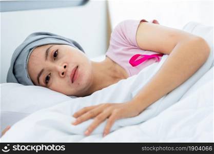 a asian women disease mammary cancer patient with pink ribbon wearing headscarf After treatment to chemotherapy lying on bed with clock and lamp In the bedroom at the house,healthcare,medicine concept