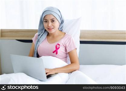 a asian women disease mammary cancer patient with pink ribbon wearing headscarf After treatment to chemotherapy with working business at laptop on bed In the bedroom at the house,healthcare,medicine