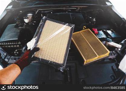 A auto mechanic holds a brand new air filter that is wrapped in plastic and a vehicle engine that has an dirty old air filter.