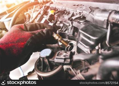 A auto mechanic is installing automobile iridium spark plugs into the ignition socket of the engine block in the engine compartment.