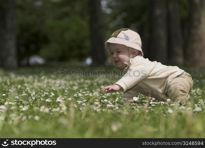 A baby is playing on a flowery meadow, exploring the surrounding nature by touching the flowers and harvesting the grass.
