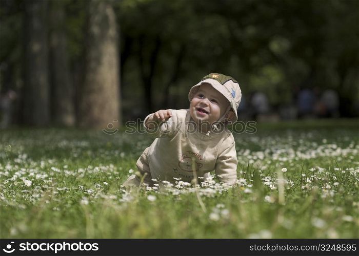 A baby is playing on a flowery meadow, exploring the surrounding nature by touching the flowers and harvesting the grass.