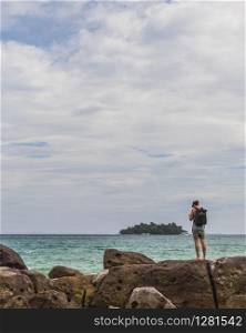 A backpacker is hiking along the coast, cloudy weather, ocean and rocks. A Hikker on Koh Rong Island, Cambodia