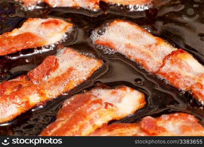 A bacon cooking detail, slices of bacon in fat