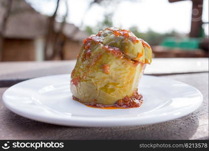 A baked green pepper with fried minceas filling, stand on a white plate on an outside table.