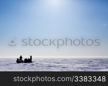 A barren flat winter landscape with two people and snowmobiles